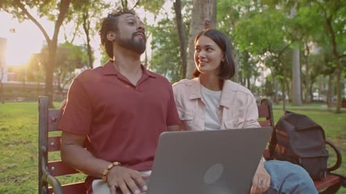 Colleagues Using Laptop and Talking in Park at Sunset