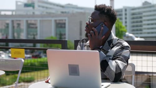 Handsome Black Man is Working with Laptop Computer in Talking By Mobile Phone in Cafe Portrait