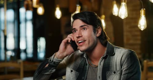 Slow motion of smiling friendly attractive young man calling his college friends in a bar. Shot in