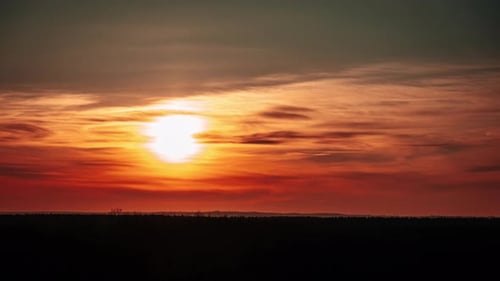Sonnenuntergang bewegt sich über dem Horizont durch Wolken im orangefarbenen Himmel im Zeitraffer