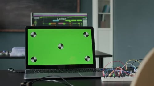 Laptop with Green Screen and Circuit Board Setup in Tech Lab