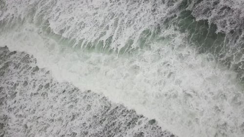 Stormy sea with waves breaking, white foam and beach sand dragged into the sea