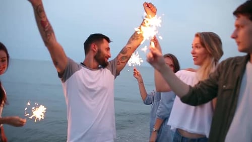 Amigos caminhando, dançando e se divertindo durante a festa noturna à beira-mar com luzes cintilantes de Bengala