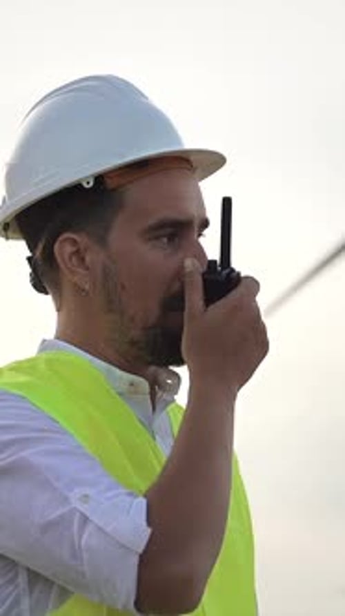 Worker Using Walkietalkie at Wind Turbine Power Station Engineer Wearing Helmet and Yellow Vest