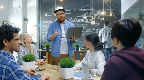 Creative Project Manager Holds Laptop and Talks to Talented Young Developers at the Team Meeting, T