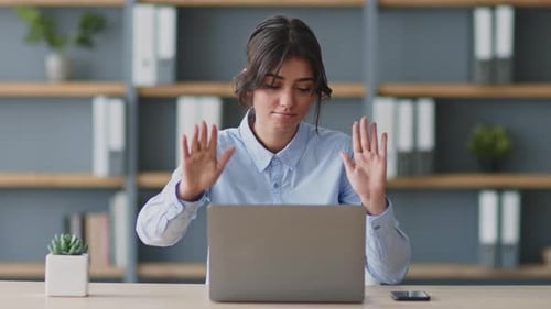 Woman Waving Hands at Desk Working on Laptop