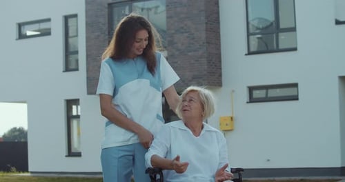 Caregiver With Senior Woman in Wheelchair Outside Home