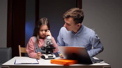 Girl Using Microscope With Man And Laptop Nearby