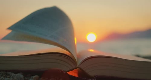 Ein offenes Buch an einem Strand bei Sonnenuntergang mit ruhigem Meer im Sommer