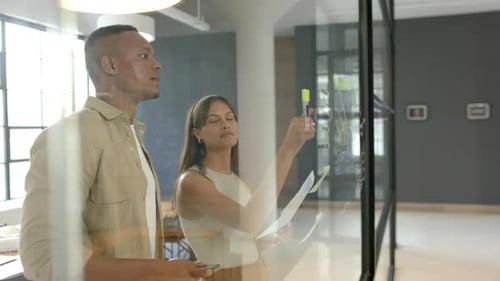 Brainstorming and writing on glass board, business colleagues discussing project in office