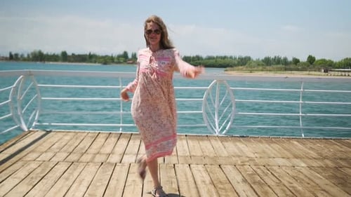 Young Generation Z woman dancing on a wooden pier enjoying freedom and fresh wind