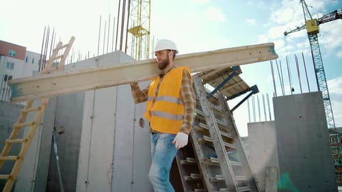 Sliding view of worker carrying long heavy beam. Frame house site building