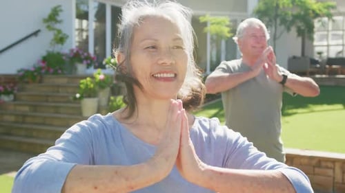 Happy diverse senior couple practicing yoga on sunny day in garden