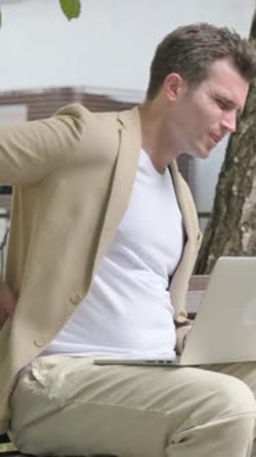 Man With Back Pain Uses Laptop Outdoors