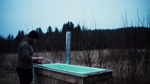 Ein Mann füllt den holzbefeuerten Whirlpool im Freien mit Wasser aus dem Schlauch. Statischer Schuss