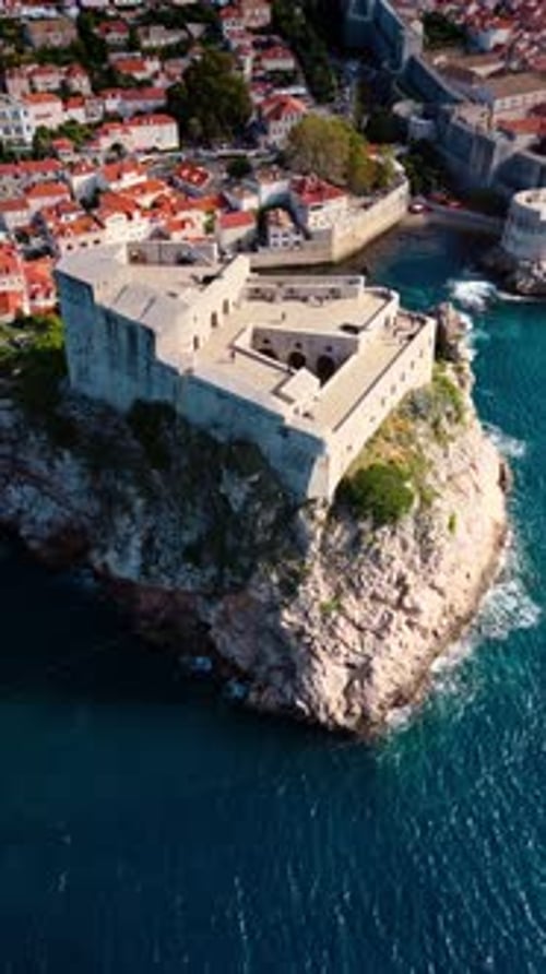 aerial portrait drone shot mid angle over fort lovrjenac on Adriatic Sea cliffs with village in sun