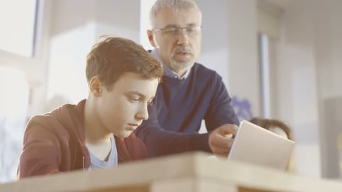 In a Computer Science Class Male Teacher Explains Programming to His Young Student.