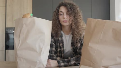 Tired Woman Staring At Groceries On Kitchen Table After Shopping Trip