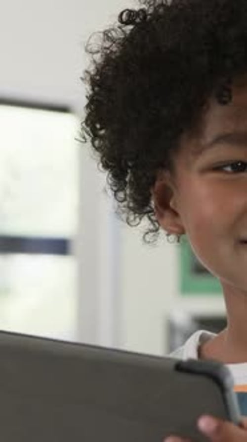 Vertical video: Smiling striped youth tapping tablet as screen drawing focus at school, copy space