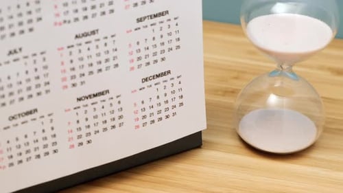 Close up of a calendar and hourglass on wooden table. Concept of starting of new year.