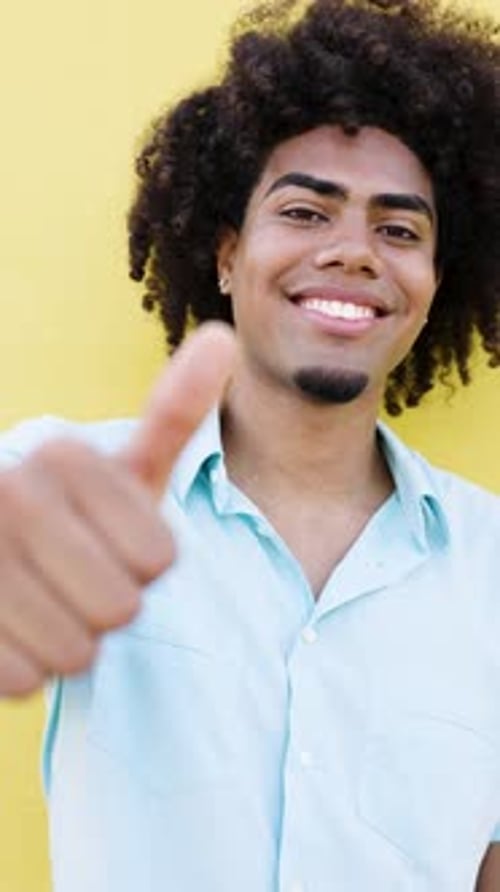 Smiling man gives a thumbs up against yellow wall