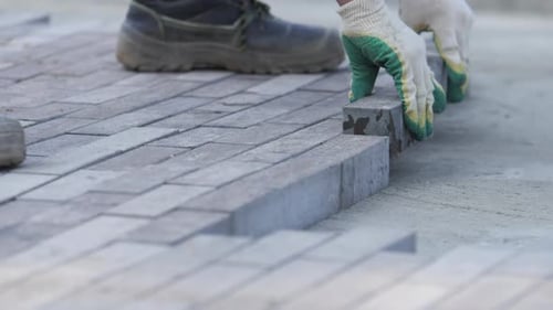 Worker in Protective Gloves Paves Pathway with Paving Tiles