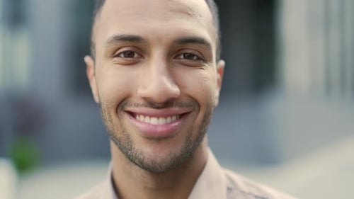 Close up portrait of a young adult man in a shirt smiling and looking at the camera. Handsome mixed