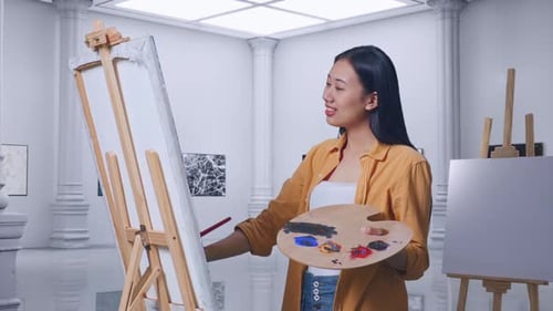 Female Using Paint Brush Measuring Picture Template While Painting On Canvas In Gallery