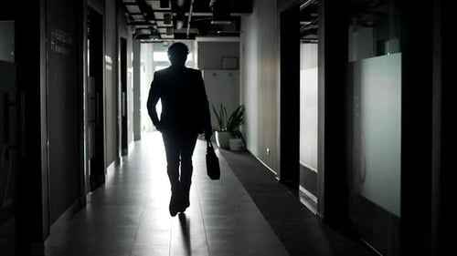 Rear view. The silhouette of a businessman in suit runs along corridor of office building.