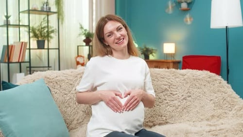 Pregnant Woman Gesturing Heart Shape on Belly on Couch