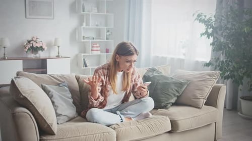 Upset Woman Using Smartphone on Couch Indoors
