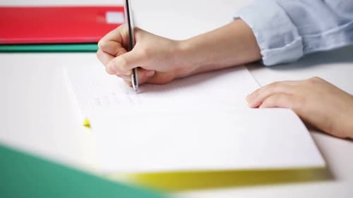Young schoolgirl hand writes math solution task to her notepad in classroom