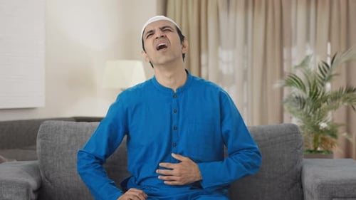 Man Experiencing Stomach Pain on Couch Indoors
