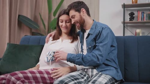 Loving Couple Holding Baby Shoes on Couch Indoors