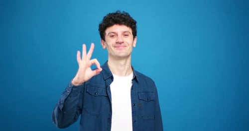 Happy Young Man Gives Okay Sign on Blue