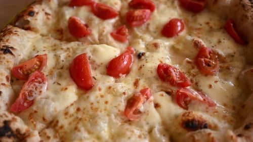Close up of freshly baked pizza topped with melted cheese and cherry tomatoes