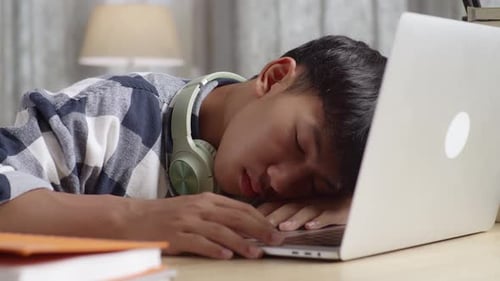 Bored Asian Teenager Yawning And Sleep At Home While Doing Home Work On Laptop Computer