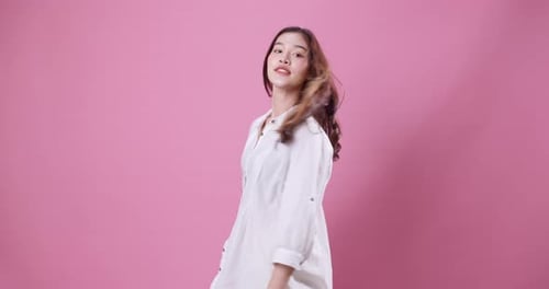 Young Asian woman moving her hair in the studio with a pink background.