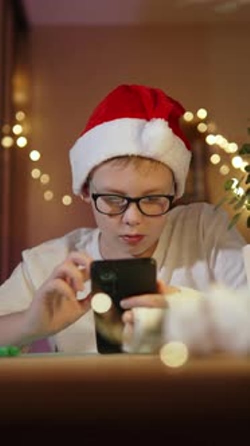 Vertical Shot of Caucasian Boy in Christmas Hat with Smartphone Tap on Screen