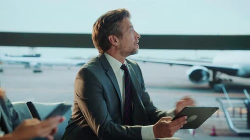 A businessman in a grey suit uses a tablet in an airport terminal