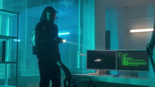 Ein Hacker in schwarzem Hoodie und Handschuhen spioniert im Labor und tippt auf einer Computertastatur