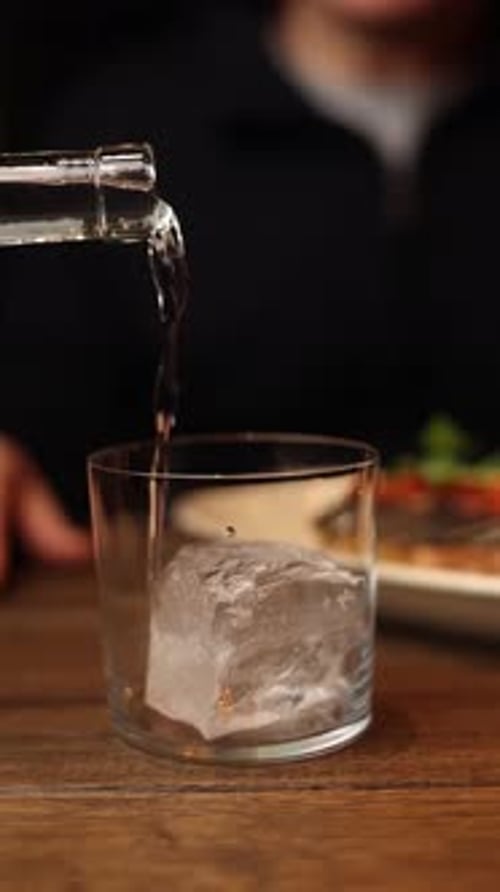A waiter is pouring alcohol into a glass with ice. Close up