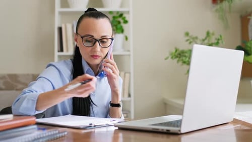 Woman Talking on Phone and Writing at Desk