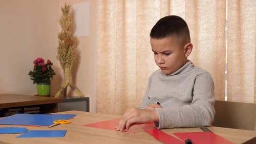 Boy Drawing on Red Paper at Wooden Table