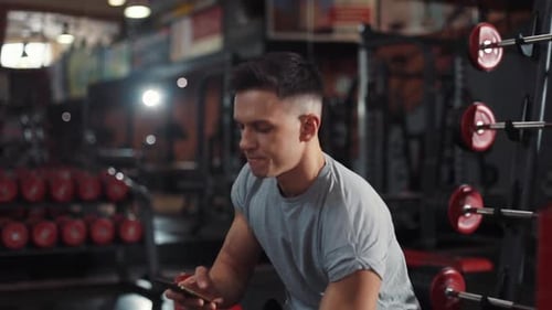 Young Man Use Phone Drink Water Look at Camera Smile in Gym Sportsman Sport Fitness Internet Face