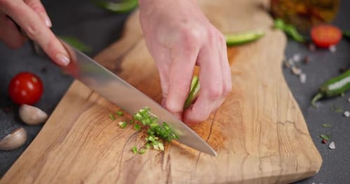 Frau schneidet grüne Chili-Pfeffer auf einem Holzschneidebrett in der Haushaltsküche