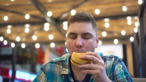 Man Eating Hamburger in Food Court Close Up