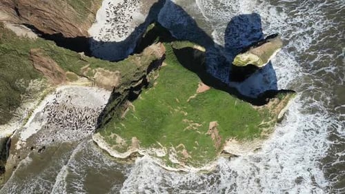 Overhead drone shot captures massive cliff towering over expansive seascape in England, UK. The rugg