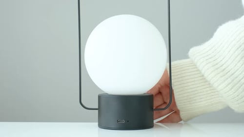 Die Hand einer Frau schaltet eine runde Lampe ein und aus, die auf einem Tisch steht.