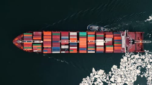 Container ship on a frozen river with ice chunks helped by a tug boat